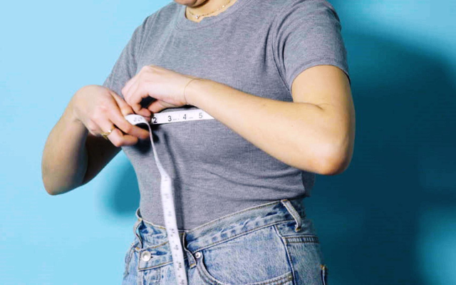 A woman uses a tape measure to determine her bra size, demonstrating a DIY bra fitting technique